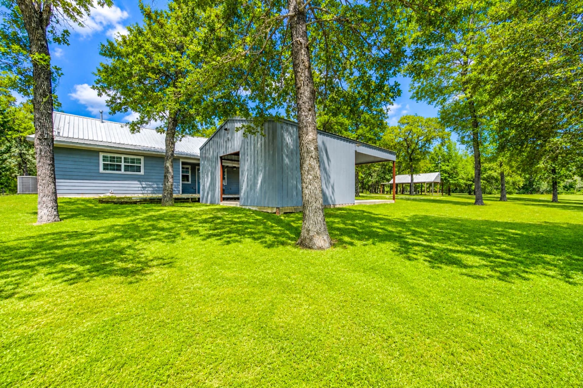Shaded backyard beneath mature oaks with the home and outbuildings
