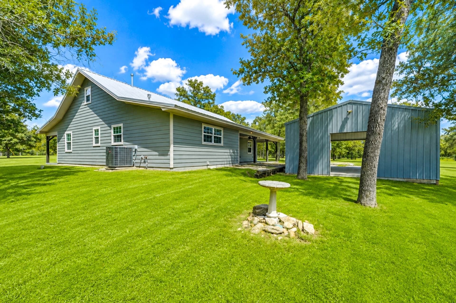 Rear of the farmhouse with standing-seam metal roof, birdbath, and metal outbuilding