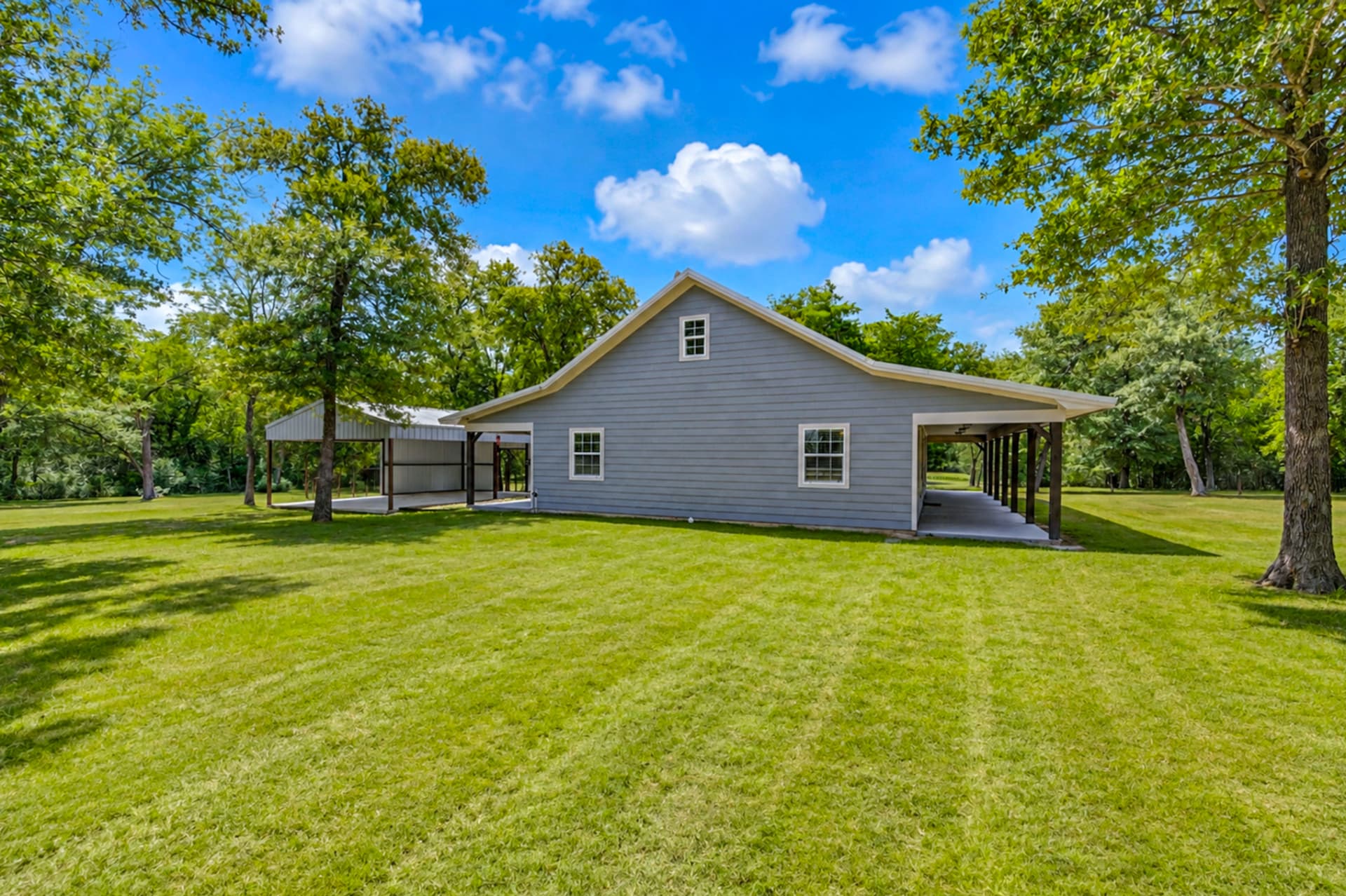 Farmhouse with attached carport and pole barn beyond the oaks